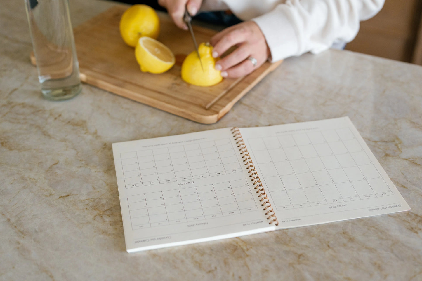 Person cutting lemons on a wooden board with a daily canvas in the foreground.