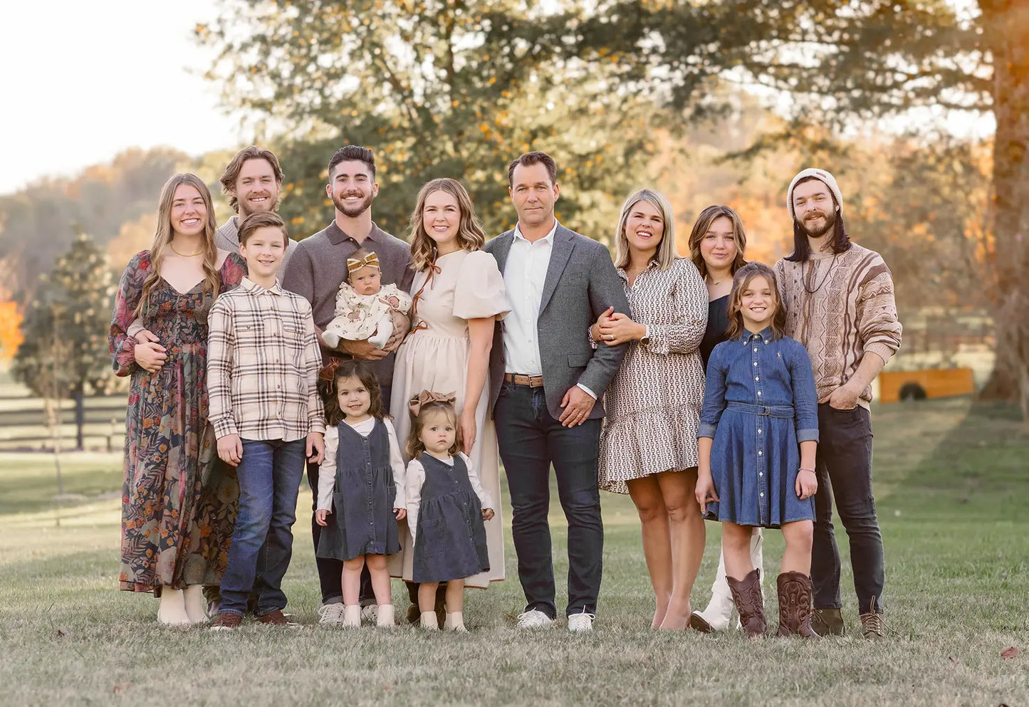 Family of 13 posing outdoors in a park-like setting with trees and grass.
