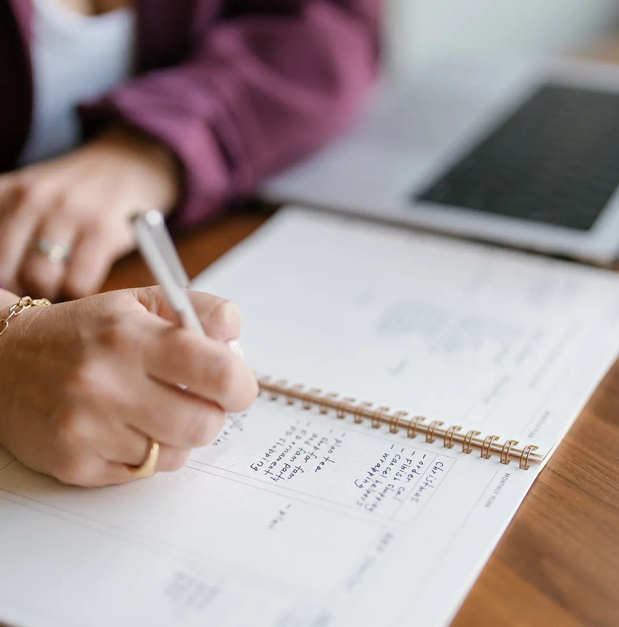Person writing in a notebook with a laptop in the background